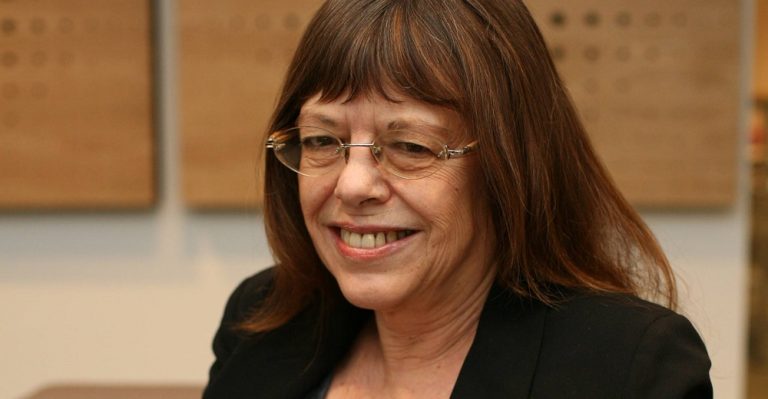 Head and shoulders photo of Diana Rose smiling at the camera with shoulder length brown hair and wearing glasses and a dark top