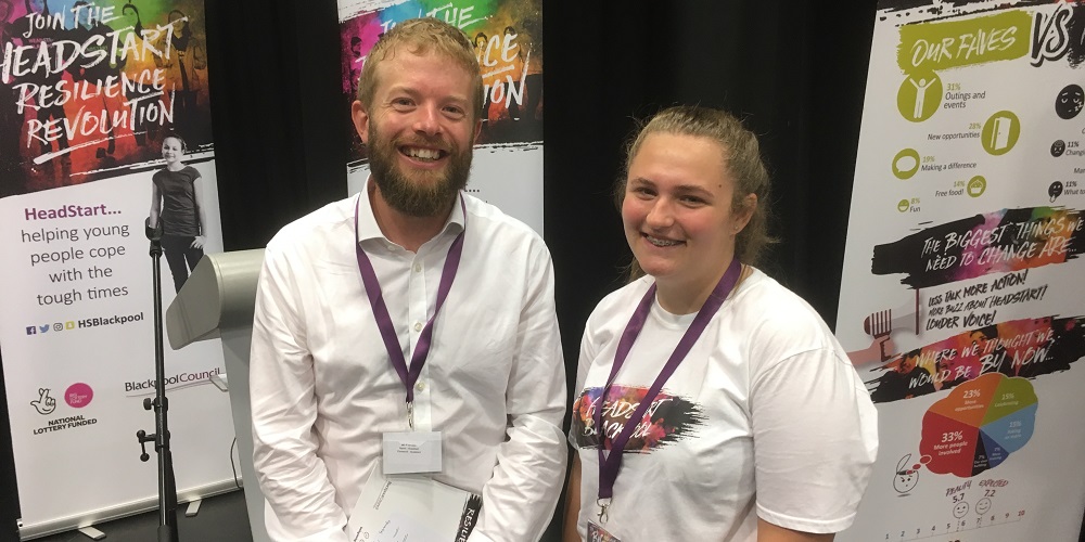 Photo of Ellie and Martin standing in front of Blackpool HeadStart banners, Ellie is on the right