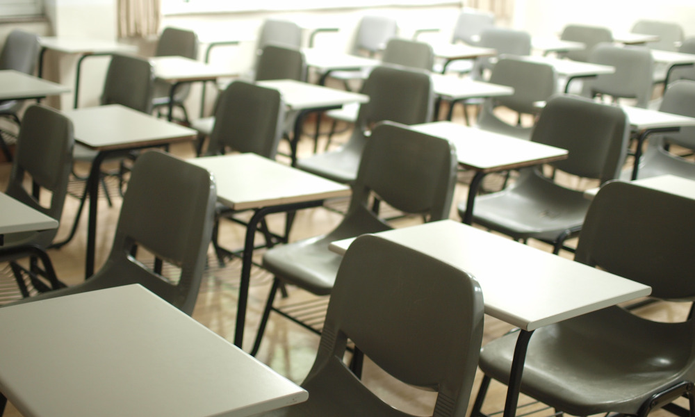 A room full of plastic chairs and individual tables laid out as for an exam