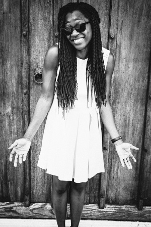 Chantel Hargreaves shrugging and smiling at the camera, wearing sunglasses and a white dress, with long hair. Chantel has written this blog on arts based approaches.