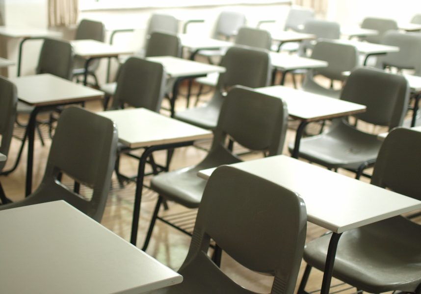 A room full of plastic chairs and individual tables laid out as for an exam